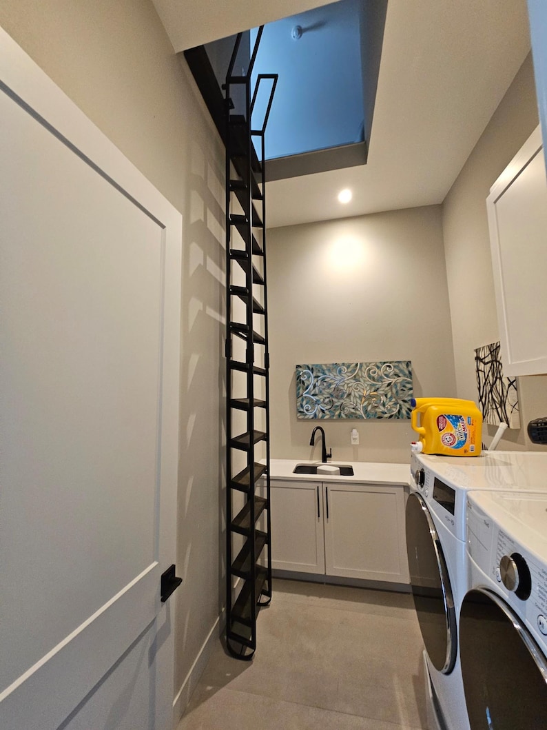 Large attic ladder with custom dark brown stained wooden treads placed in a residential laundry room