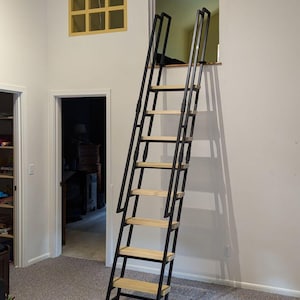 Room 62s custom loft ladder for residential home. This ladder is our standard black frame with poplar wooden treads and grab rails. The ladder leads into a crawlspace opening.