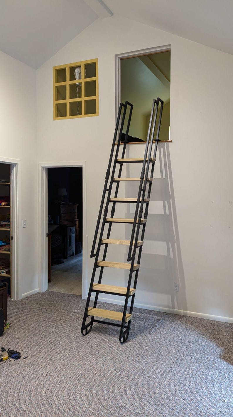 Room 62s custom loft ladder for residential home. This ladder is our standard black frame with poplar wooden treads and grab rails. The ladder leads into a crawlspace opening.