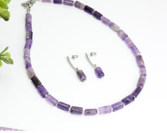 Könnte beinhalten: Ein violettes Amethyst-Halsketten- und Ohrring-Set. Die Halskette besteht aus facettierten Amethystperlen und einer silbernen Kette. Die Ohrringe sind silberfarben mit Amethyst-Tropfen.