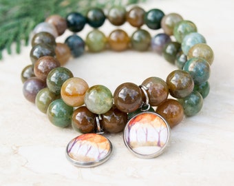 May include: A double-strand bracelet made of green, brown, and beige agate beads with two round charms featuring watercolor paintings of trees.