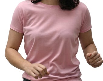 May include: A light pink crew neck t-shirt. The short-sleeved shirt is made of a soft material and is a solid color. The person is wearing blue jeans. The background is white.