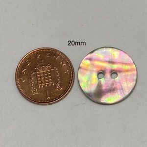 May include: A round, iridescent button with two holes, approximately 20mm in diameter, next to a penny. The button has a pearlescent sheen with colours ranging from yellow to purple.