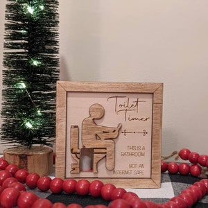 May include: A wooden sign with a silhouette of a person sitting on a toilet. The sign reads "Toilet Timer" and "This is a bathroom, not an internet cafe".