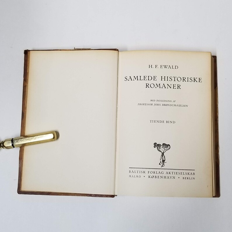 Puede incluir: Un libro abierto con una cubierta de cuero marr&oacute;n y p&aacute;ginas color crema. El t&iacute;tulo en la p&aacute;gina derecha dice "SAMLEDE HISTORISKE ROMANER" de H.F. Ewald. El libro es de Baltisk Forlag Aktieselskab, con ubicaciones en Malm&ouml;, Copenhague y Berl&iacute;n.
