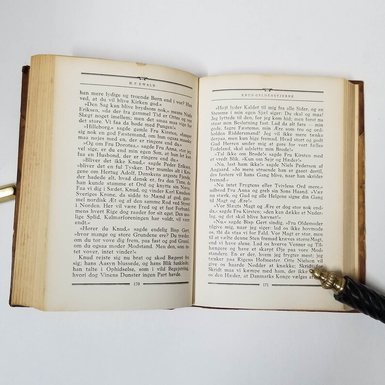 Puede incluir: Un libro abierto con p&aacute;ginas envejecidas, con texto en una fuente cl&aacute;sica. Una pluma descansa sobre la p&aacute;gina y la portada del libro es visible. El libro es probablemente un texto hist&oacute;rico o una novela.