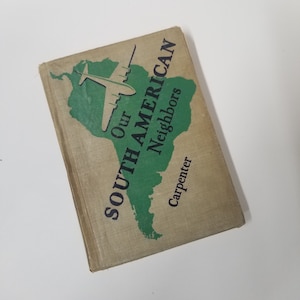 May include: Vintage book titled "Our South American Neighbors" by Carpenter. The cover features a green map of South America with a white airplane illustration. The title is in dark blue, and the book has a tan cover.