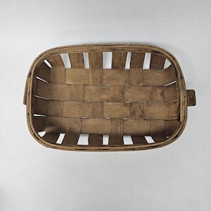 May include: An oval-shaped woven basket constructed from thin, flat strips of brown wood. The basket features a grid-like pattern created by the interlaced horizontal and vertical wooden slats, forming an open, sturdy structure with a rim.