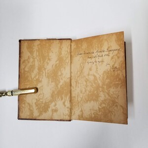 Puede incluir: Un libro antiguo abierto con p&aacute;ginas envejecidas y veteadas. Las p&aacute;ginas interiores son de color marr&oacute;n c&aacute;lido con un patr&oacute;n arremolinado. Se ve texto manuscrito en la p&aacute;gina derecha. La cubierta del libro es de color marr&oacute;n oscuro.