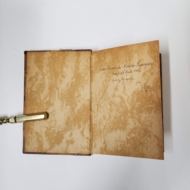 Puede incluir: Un libro antiguo abierto con p&aacute;ginas envejecidas y veteadas. Las p&aacute;ginas interiores son de color marr&oacute;n c&aacute;lido con un patr&oacute;n arremolinado. Se ve texto manuscrito en la p&aacute;gina derecha. La cubierta del libro es de color marr&oacute;n oscuro.