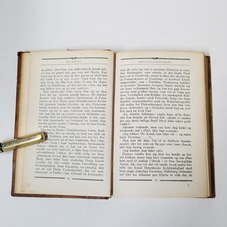 Puede incluir: Un libro abierto con texto en p&aacute;ginas envejecidas, con un bol&iacute;grafo dorado en el lado izquierdo. La portada del libro es de color marr&oacute;n oscuro y las p&aacute;ginas est&aacute;n amarillentas.