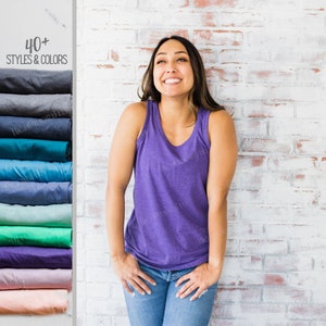May include: A woman wearing a purple tank top and blue jeans stands in front of a white brick wall. The text "40+ Styles & Colors" is visible in the upper left corner of the image.