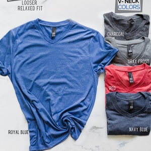 May include: A variety of V-neck t-shirts in different colors, including royal blue, charcoal, red, gray frost, and navy blue. The shirts are made of a soft, comfortable fabric and have a looser, relaxed fit.  Unisex.