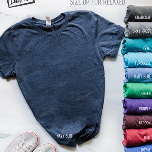 May include: A navy blue t-shirt with the text "Semi-fitted Ladies" and "Runs Small... Size Up For Relaxed" on a white background. The t-shirt is folded and displayed with a variety of color options.
