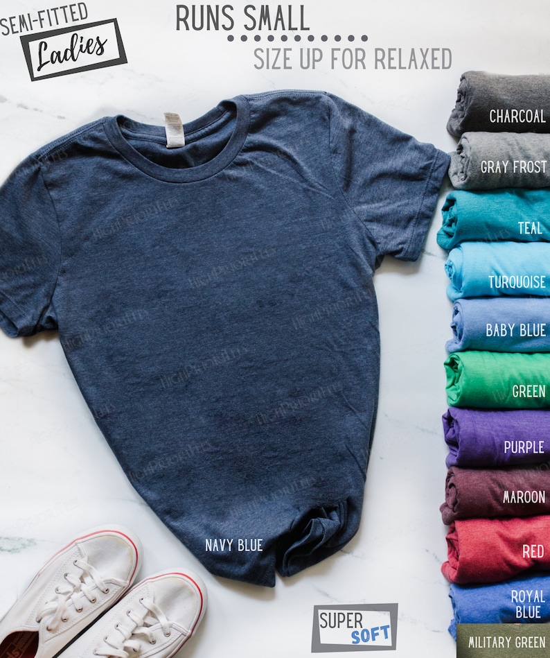 May include: A navy blue t-shirt with the text "Semi-fitted Ladies" and "Runs Small... Size Up For Relaxed" on a white background. The t-shirt is folded and displayed with a variety of color options.
