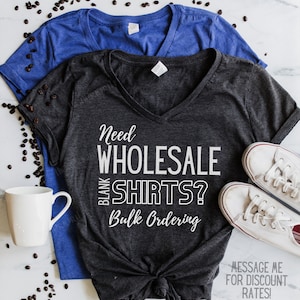 May include: A dark gray V-neck t-shirt with the text "Need Wholesale Blank Shirts? Bulk Ordering" in white. The text "Message me for discount rates! Minimum Qty 15 Save 20 - 50%!". is also printed on the shirt.