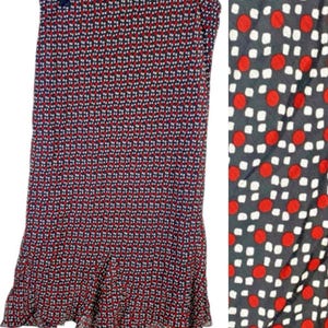May include: A long, flowing skirt with a repeating pattern of red dots and white squares on a navy blue background. The skirt has a ruffled hemline and is hanging on a wooden hanger.
