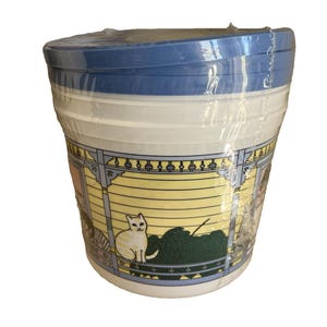 May include: A stack of white plastic bowls with a blue lid, wrapped in clear plastic. The bowls have a decorative band featuring a cat, yarn, and a yellow and blue house design.