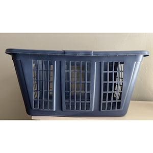 May include: A navy blue plastic laundry basket with a rectangular shape. The basket has a series of rectangular openings on the front and sides for ventilation. The top edge has a handle for easy carrying. This laundry basket is designed for storing and transporting clothes.