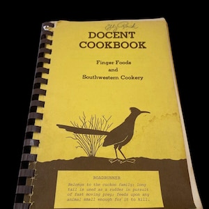 May include: A yellow cookbook with a brown border and a black and white illustration of a roadrunner. The title of the book is "DOCENT COOKBOOK" with the words "Finger Foods and Southwestern Cookery" below the title. The text below the illustration reads "ROADRUNNER Belongs to the cuckoo family; long tail is used as a rudder in pursuit of fast moving prey; feeds upon any animal small enough for it to kill."