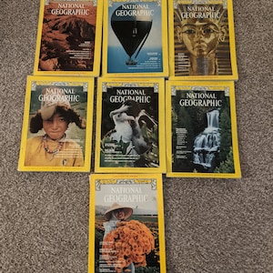 Puede incluir: Una colección de revistas National Geographic vintage con portadas amarillas y una pancarta roja con el nombre de la revista. Las portadas presentan una variedad de imágenes, incluyendo un globo aerostático, una cascada, una mujer sosteniendo flores y un retrato de una persona indígena.