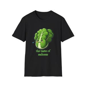May include: Black t-shirt with a cartoon illustration of a green leafy vegetable with a sad face and a single tear. The text "the taste of sadness" is printed below the vegetable.