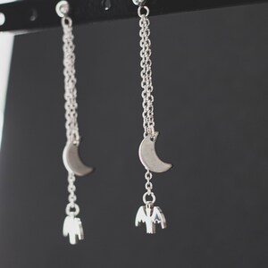 May include: Silver dangle earrings with a crescent moon charm and a bat charm hanging from the bottom.