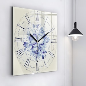 Puede incluir: Un reloj cuadrado de vidrio con fondo blanco y diseño floral azul. La esfera del reloj tiene números romanos y una aguja de hora y minutos negra.