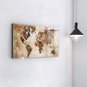 Pode incluir: Um relógio de parede retangular com um design de mapa do mundo em um fundo marrom e bege. O mostrador do relógio tem números e ponteiros brancos.