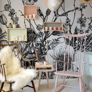 Op de afbeelding: Een zwart-witte bloemenbehang met een roze schommelstoel en een houten bijzettafel. Het behang heeft een groot bloemenmotief met takken en bladeren. De schommelstoel is van hout en heeft een roze afwerking. De bijzettafel is van hout en heeft een natuurlijke afwerking. De tekst "RetRoll Interiors" is zichtbaar in de linkerbenedenhoek van de afbeelding.