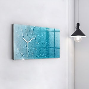 Può includere: Un orologio in vetro blu e bianco con un design a goccia d'acqua. L'orologio ha lancette argentate e un quadrante bianco.