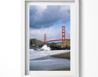 May include: A photograph of the Golden Gate Bridge in San Francisco, California. The bridge is red and spans a body of water. The water is choppy and whitecaps are visible. The sky is cloudy and gray.