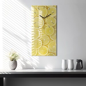 Puede incluir: Un reloj de vidrio amarillo con una esfera y agujas negras. La esfera está rodeada por un patrón de rodajas de limón amarillas.