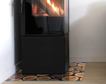 May include: A black metal fireplace with a glass door containing a burning log fire. Beneath the fireplace sits a rectangular floor plate featuring a repeating pattern of circular wood grain slices in brown and tan tones.