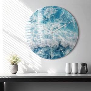 Può includere: Un orologio da parete rotondo con un design a onde oceaniche blu e bianche. L'orologio ha lancette bianche e un centro dorato.