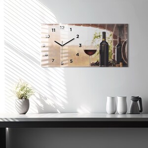 May include: A clock with a wine glass and bottles of wine in the background. The clock face is white with black numbers and hands. The background is a blurry image of a vineyard.