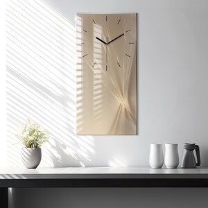 Op de afbeelding: Een beige en gouden abstracte wandklok met zwarte wijzers. De klok heeft een modern ontwerp met een draaiend patroon.