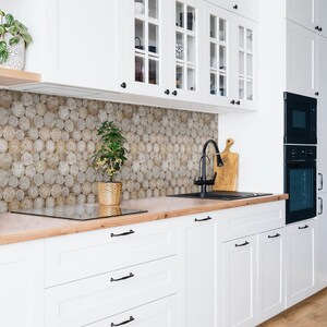 Könnte beinhalten: Weiße Küchenschränke mit Glastüren und schwarzen Beschlägen. Die Arbeitsplatte ist aus Holz und hat ein schwarzes Spülbecken und einen schwarzen Wasserhahn. Auf der Arbeitsplatte steht eine kleine Pflanze in einem braunen Topf.