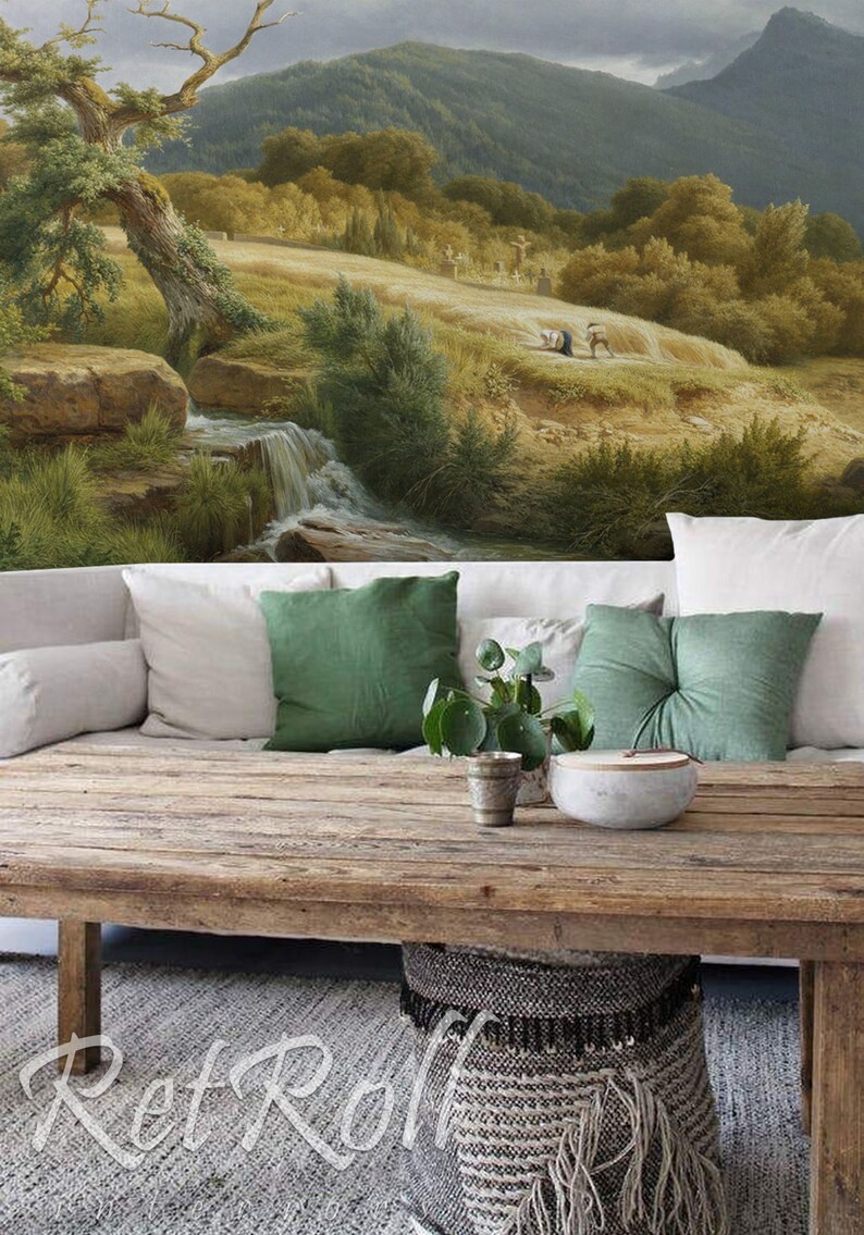 Op de afbeelding: Een rustieke houten salontafel met een landschapsschildering op de achtergrond. De tafel is versierd met witte en groene kussens, een kleine plant en een decoratieve kom. Onder de tafel staat een geweven mand.