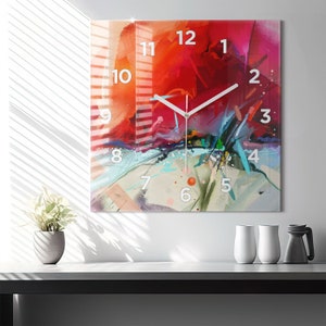 Könnte beinhalten: Eine quadratische Uhr mit einem abstrakten Design in Rot, Orange, Blau und Weiß. Das Zifferblatt der Uhr hat weiße Zahlen und Zeiger.