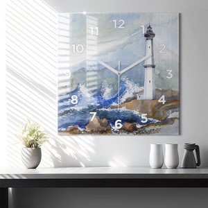 Puede incluir: Una pintura de acuarela de un faro en una costa rocosa con olas rompiendo. El faro es blanco con una parte superior negra y una franja negra alrededor del medio. Las olas son azules y blancas, y las rocas son marrones. La pintura está enmarcada en un marco de vidrio transparente y tiene una esfera de reloj con números romanos.
