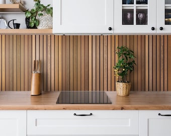 May include: White kitchen cabinets with black hardware above a wood slat backsplash. A black electric stovetop is on the counter with a small potted plant to the right.