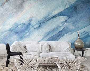 May include: A wall mural featuring a blue and gray watercolor wash pattern behind a white sofa, two white wire chairs, a black chair, a wooden coffee table, a glass bottle lamp, and a shaggy rug on a light wood floor.