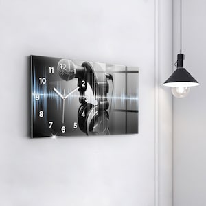 Puede incluir: Un reloj en blanco y negro con un micrófono y auriculares. La esfera del reloj tiene un fondo blanco con números y manecillas negros. El micrófono está en la esquina superior izquierda de la esfera del reloj. Los auriculares están en la esquina inferior derecha de la esfera del reloj. El reloj está configurado a las 10:10.