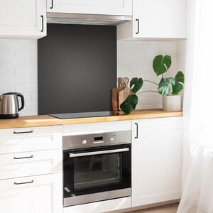May include: A white kitchen with a stainless steel oven and a black stovetop. The kitchen has white cabinets and a wooden countertop. There is a plant on the counter and a white tiled backsplash.