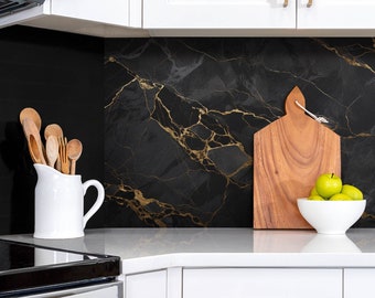 May include: Black and gold marble kitchen backsplash with a white countertop, a white pitcher with wooden spoons, a wooden cutting board, and a white bowl with green apples.