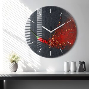 Könnte beinhalten: Eine runde schwarze Uhr mit weißen Zeigern und Zahlen. Das Zifferblatt der Uhr zeigt eine rote Chilischote und rote Chiliflocken, die um sie herum verstreut sind.