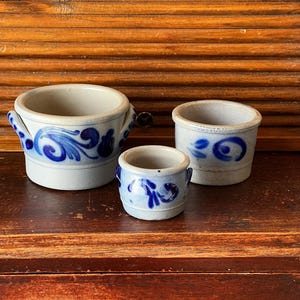 May include: Three antique stoneware pots with blue floral patterns. The pots are of different sizes, the largest with handles. The blue and white colour scheme gives them a rustic, vintage aesthetic. These decorative pots are ideal for displaying small plants or as decorative accents.
