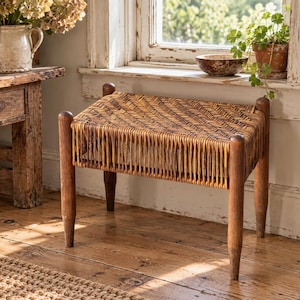 May include: A rectangular footstool featuring four dark brown wooden legs and a woven rattan seat with a herringbone pattern. The stool has a sturdy frame with vertical rattan slats connecting the seat to the base of the legs.