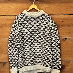 Peut inclure: Un pull beige et marron à motifs avec un col rond. Le pull est suspendu à un cintre en bois sur un fond en bois. Le motif est un motif de losanges répétés en marron et beige.